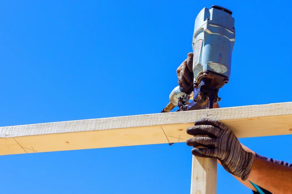 closeup of gloved hands using a nail gun on a construction site