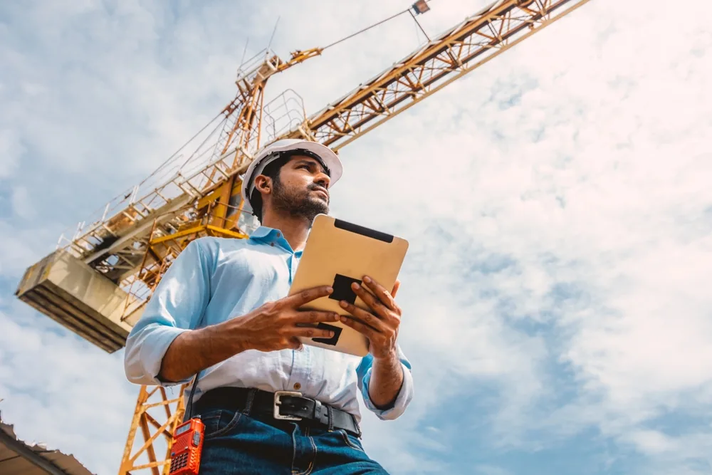 building inspector writes a report under a crane on a construction site
