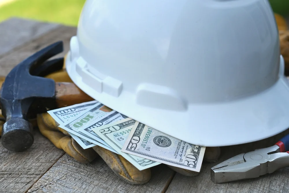 Construction hat on top of dollar bills, construction worker paid in cash.