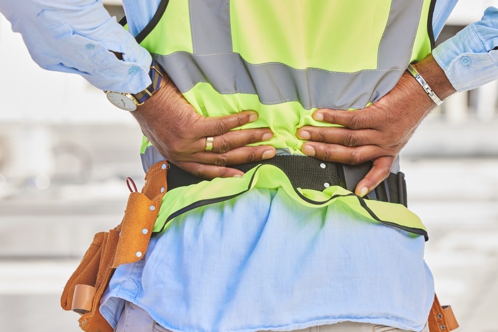 Zoom a un trabajador de construcción agarrándose la espalda con dolor.