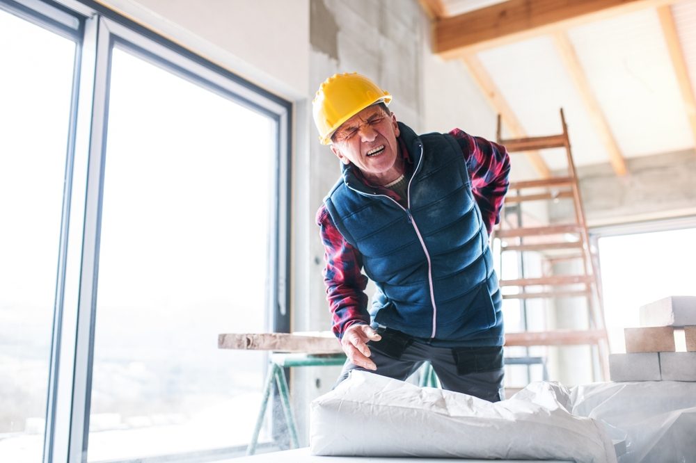 Trabajador de construcción se agarra la espalda con dolor.