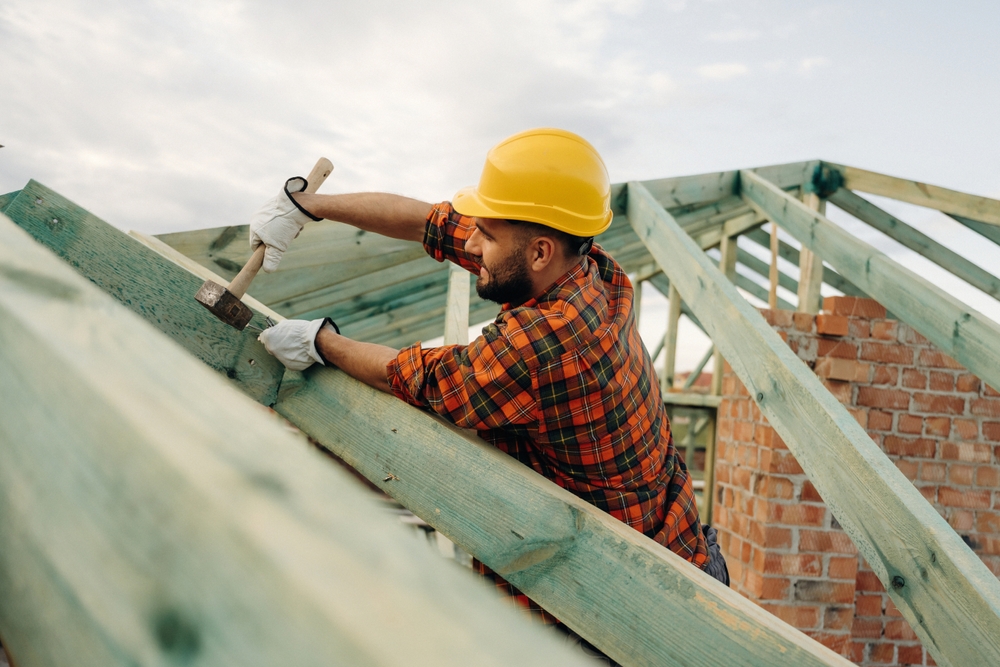 Construction worker works with a hammer on a roof.