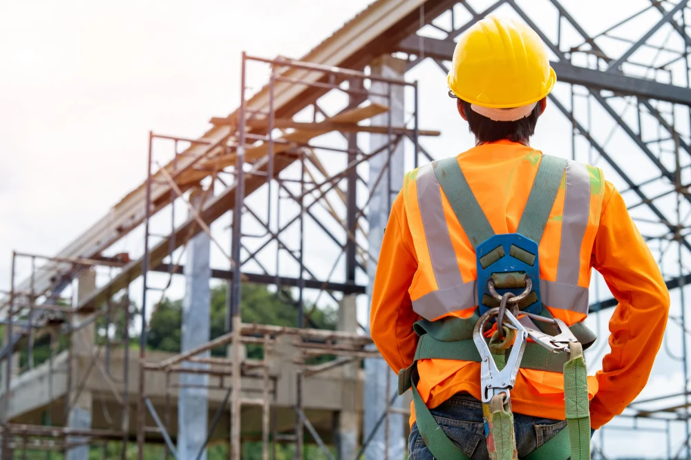 Construction worker wearing protective gear looks on to an elevated metal structure