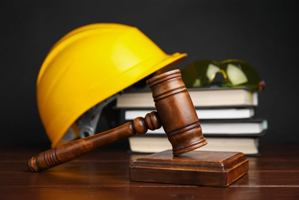 Workers compensation concept, gavel, books and construction worker protective gear on a wooden table